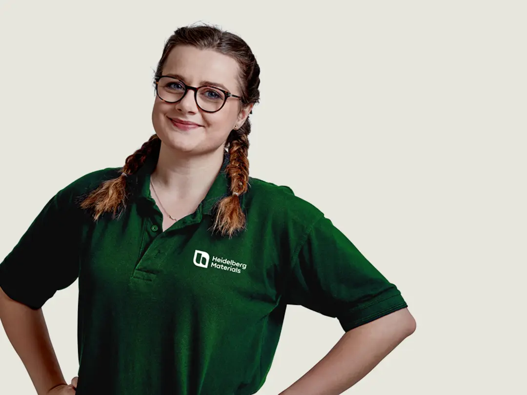 Person wearing a green polo shirt with embroidered company logo, standing confidently with hands on hips against a plain background.